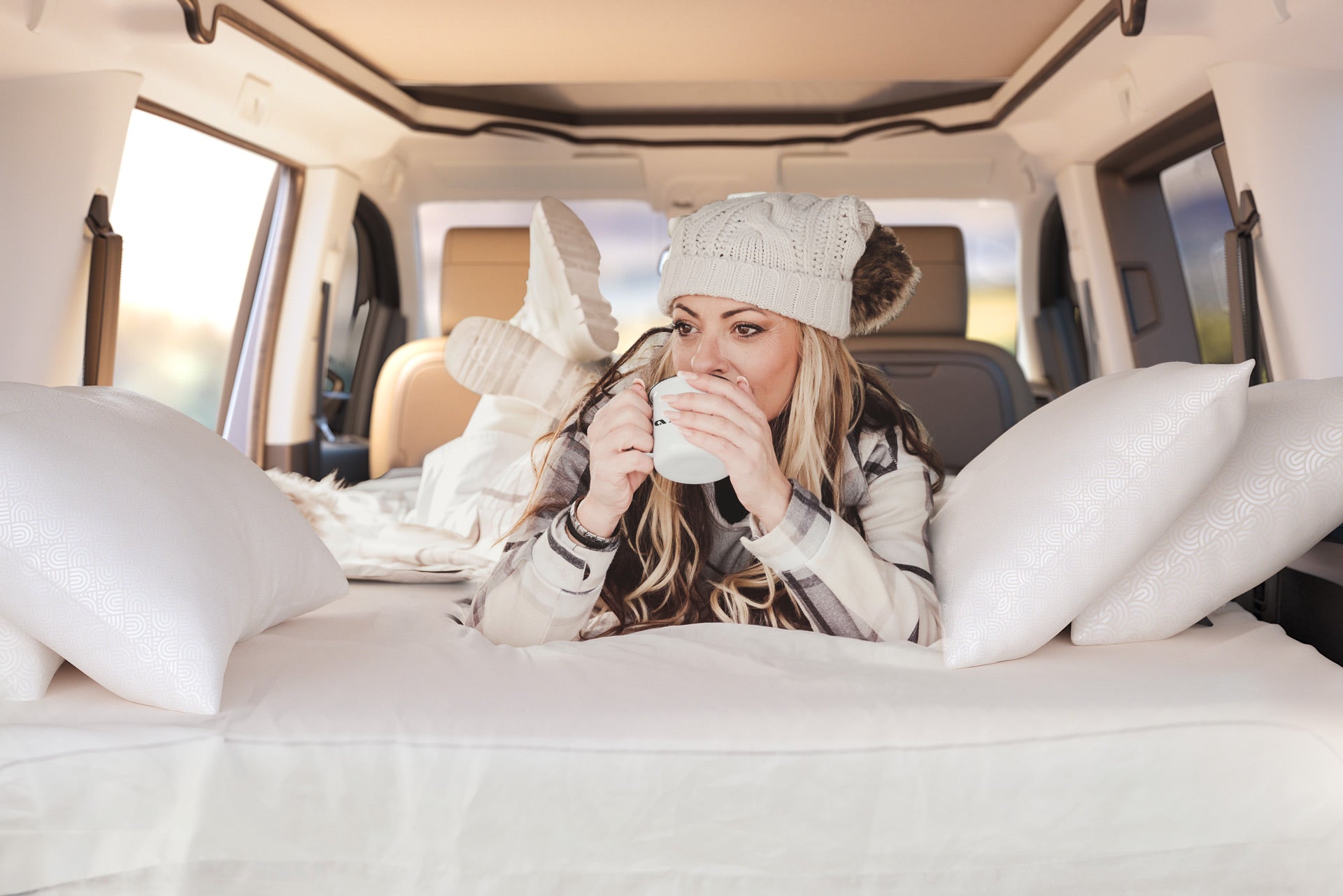 Image creation-A woman sitting in the back of a car surrounded by pillows, holding a cup of coffee.